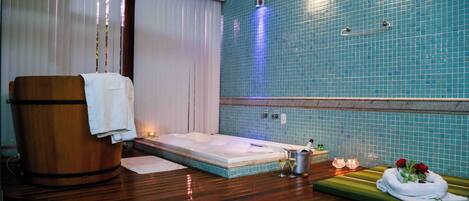 Ein Spa-Raum mit einer Holzwanne, einer Massageliege und einer Wand mit blauen Fliesen.