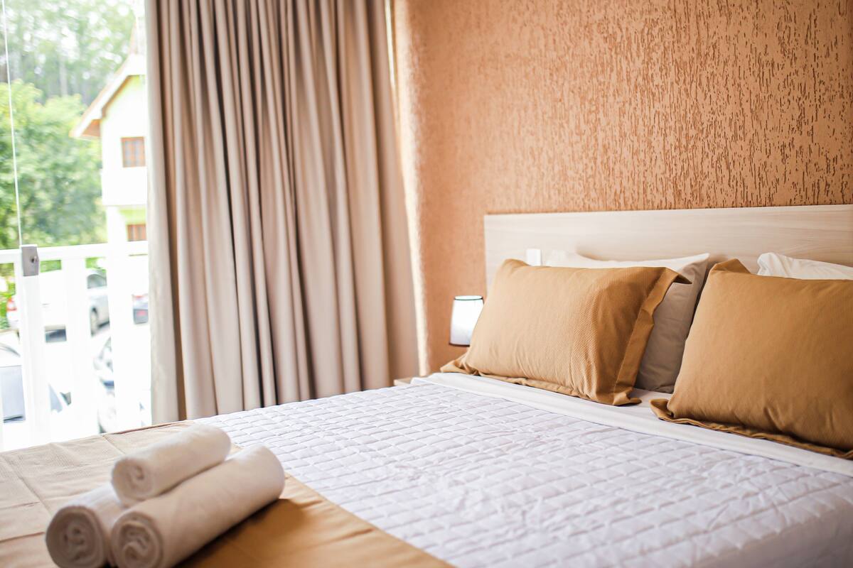 Een hotelkamer met een bed, gordijnen en uitzicht op gebouwen.