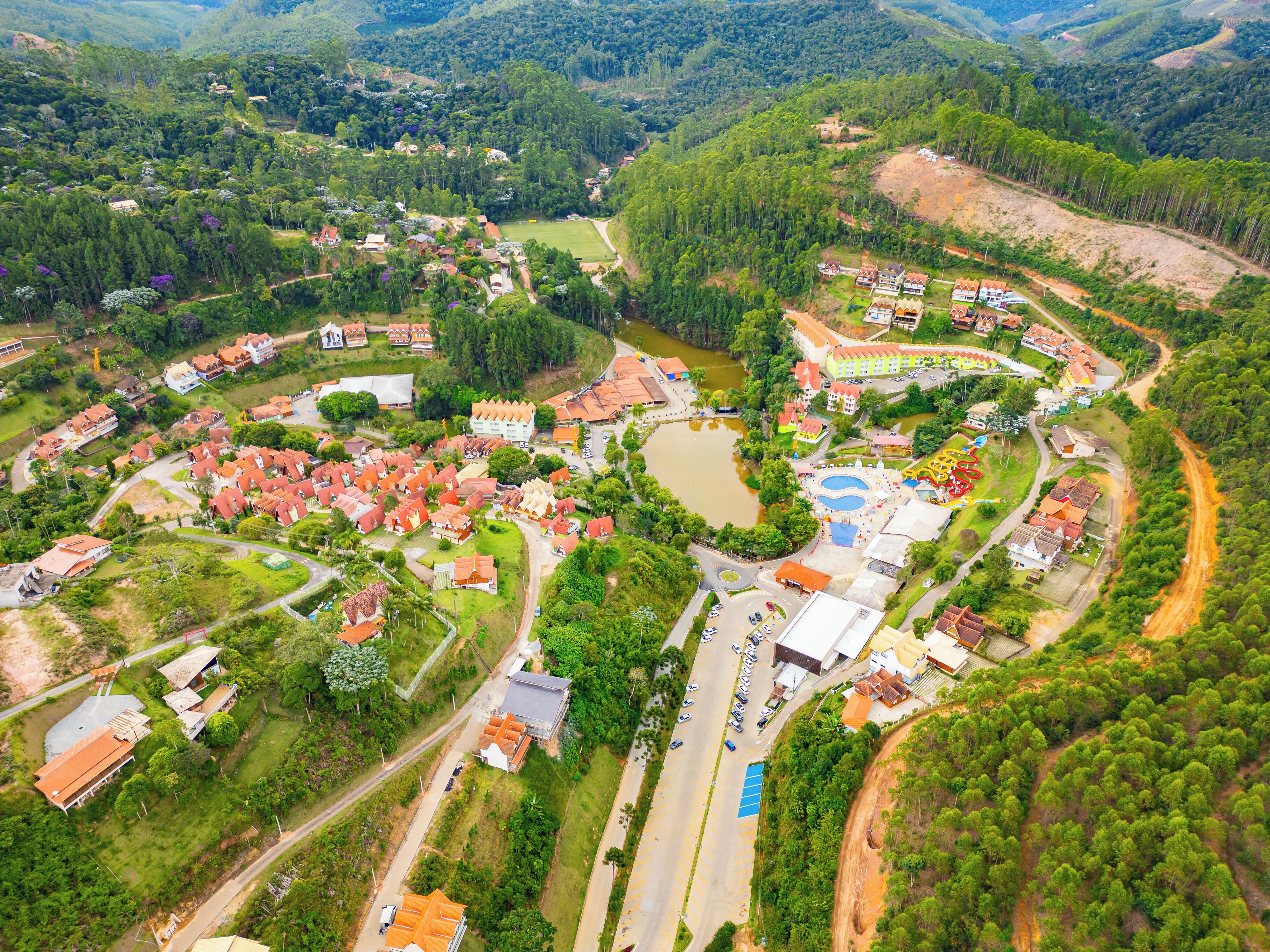 An aerial view of a resort with multiple buildings, a swimming pool, and a surrounding natural landscape.