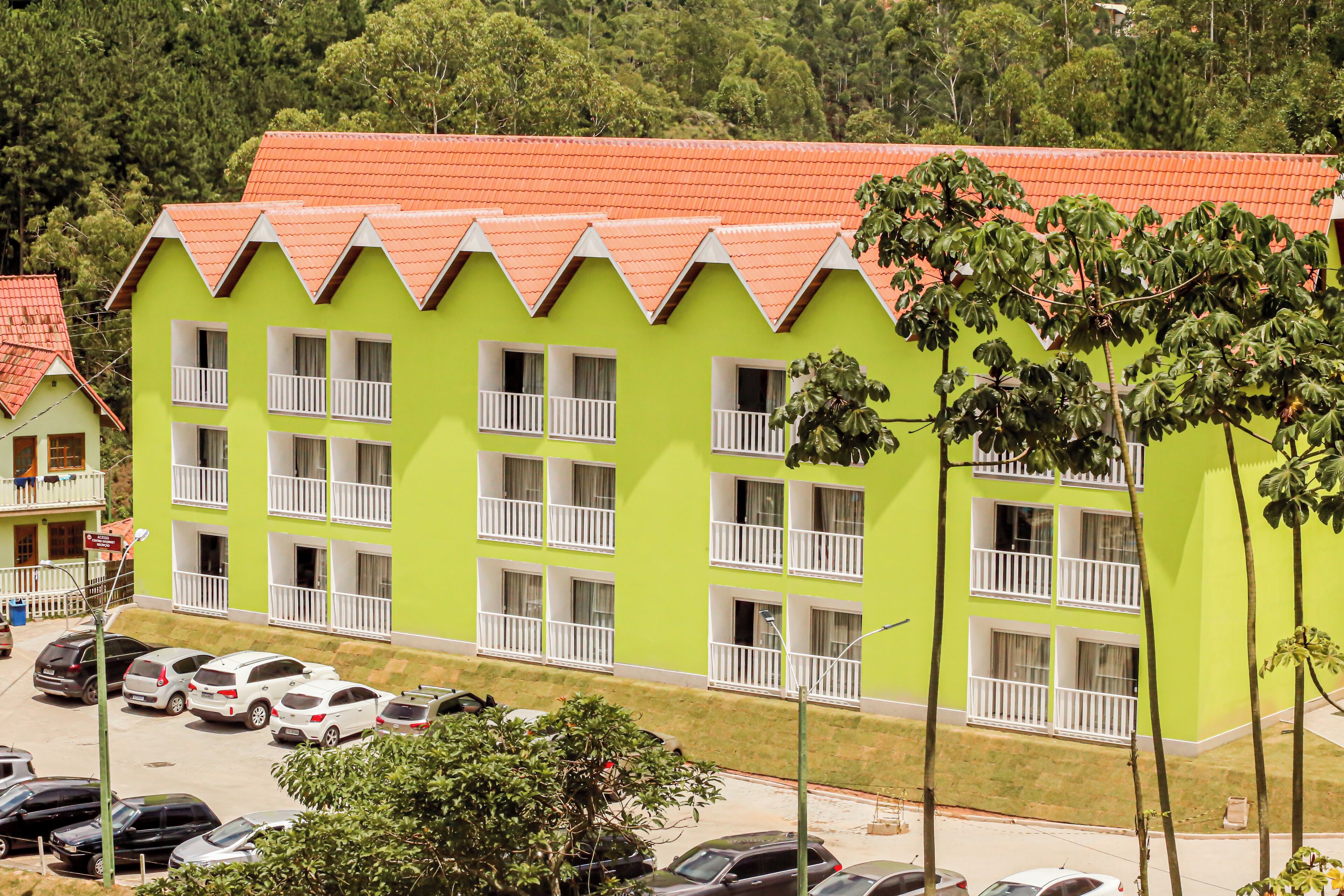 Un edificio de varios pisos con fachada verde brillante y techo rojo. Cuenta con balcones con barandillas blancas y numerosas ventanas.