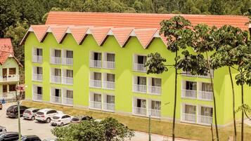 Un edificio de varios pisos con fachada verde brillante y techo rojo. Cuenta con balcones con barandillas blancas y numerosas ventanas.