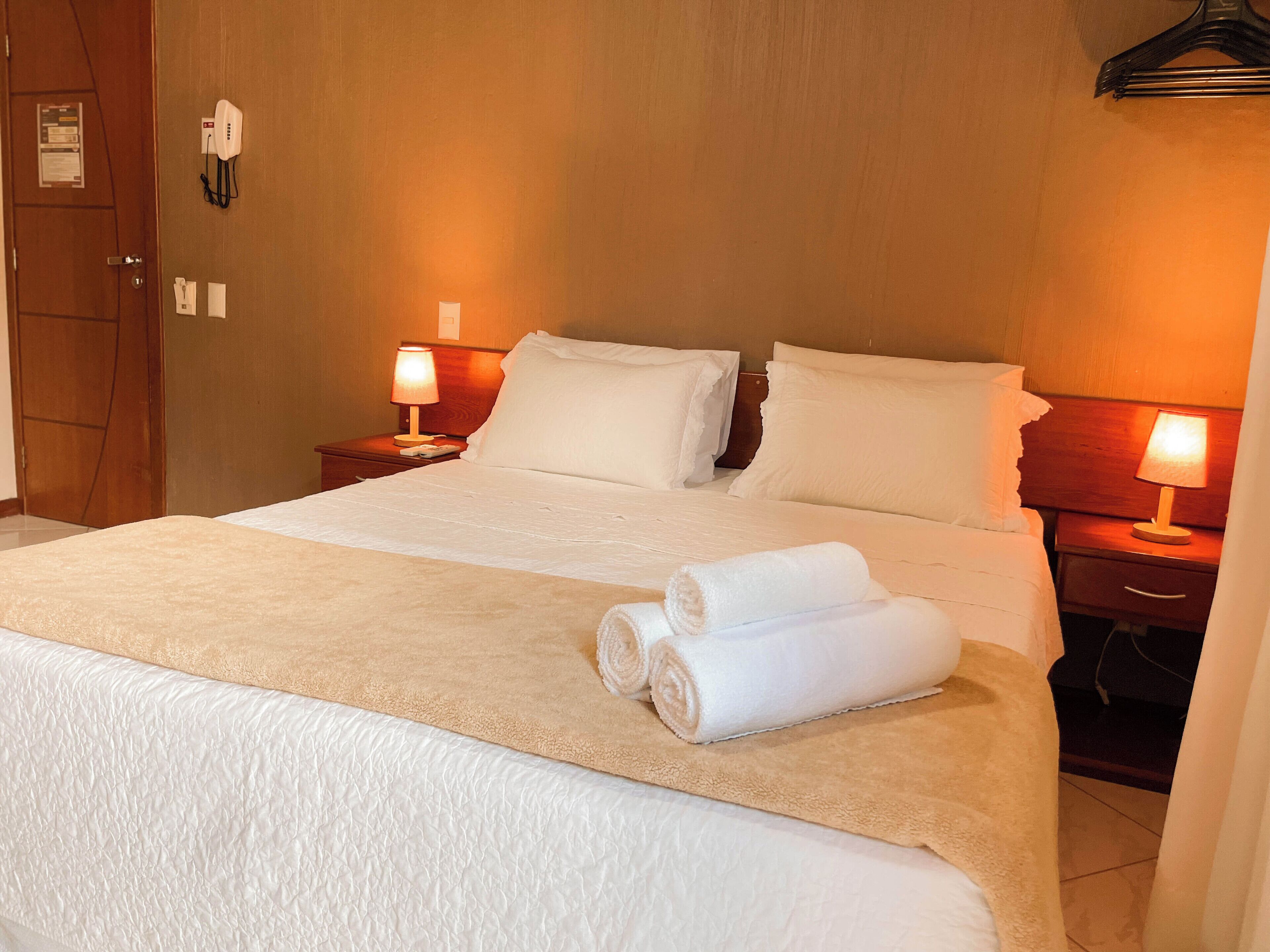 A neatly made bed with white linens and two bedside lamps.
