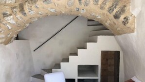 A staircase leading to a loft area with a stone archway, a white chair, and a white sofa with a striped pillow. - La Petite Maison (Montaulieu)