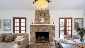 A living room with a stone fireplace, leather sofa, dining table with chairs, and a chandelier. - Large deck, open floor plan, walk to shopping. (Carmel By the Sea)