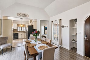 A dining area with a wooden table set for four, a vase with flowers, and a kitchen in the background. - Large deck, open floor plan, walk to shopping. (Carmel By the Sea)