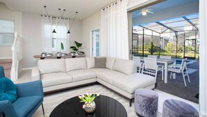 Un salon moderne avec un canapé d’angle, une table basse agrémentée de fleurs et un coin repas avec des sièges d’extérieur.