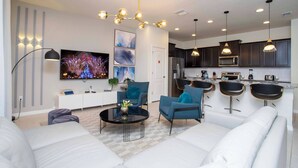 Un salon moderne avec un téléviseur à écran plat, une table basse et des fauteuils bleus.