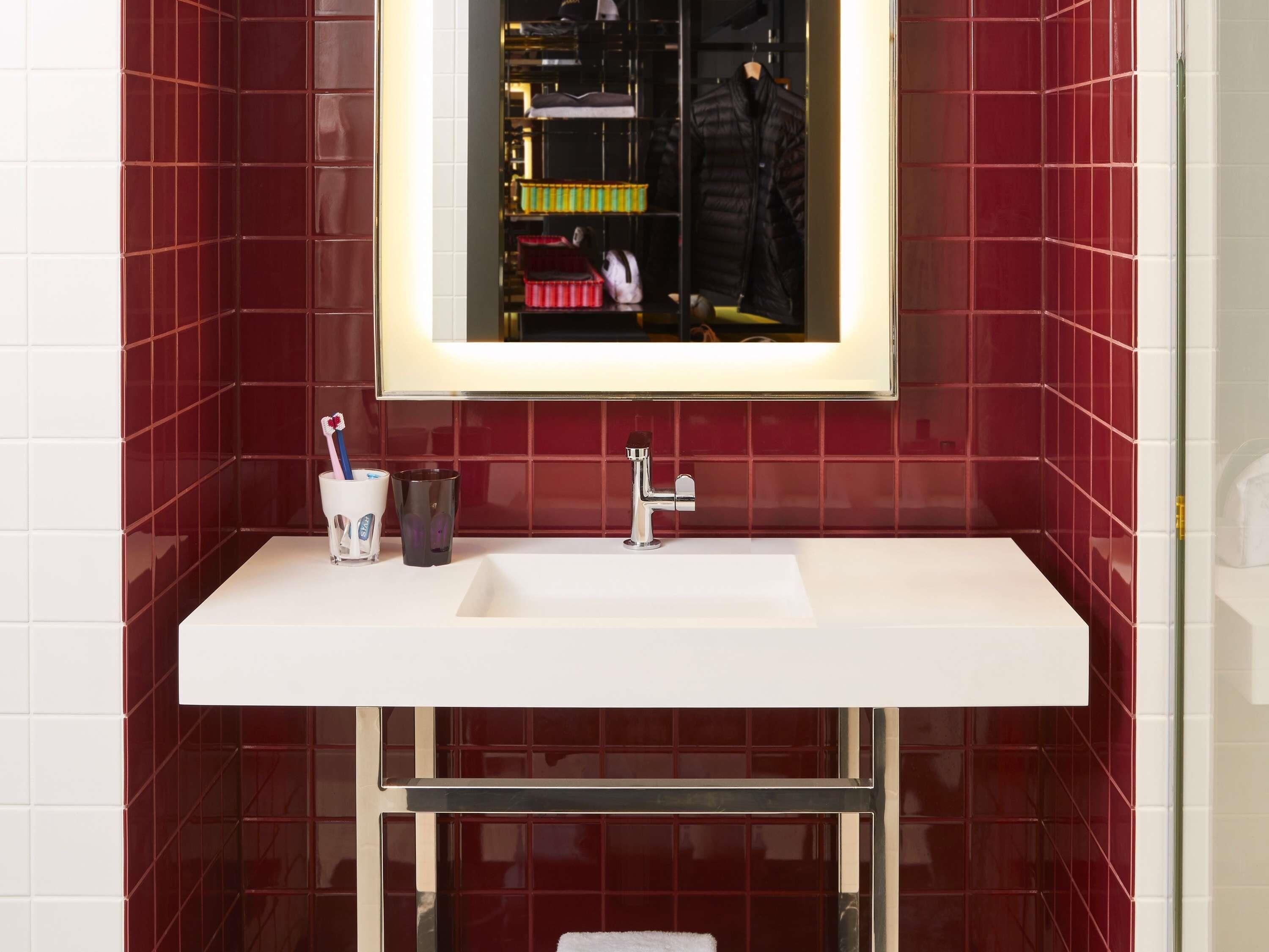 Un baño con un lavabo blanco, un espejo y paredes de azulejos rojos.