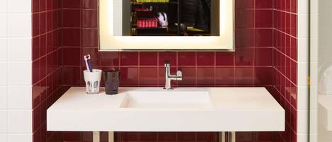 Un baño con un lavabo blanco, un espejo y paredes de azulejos rojos.