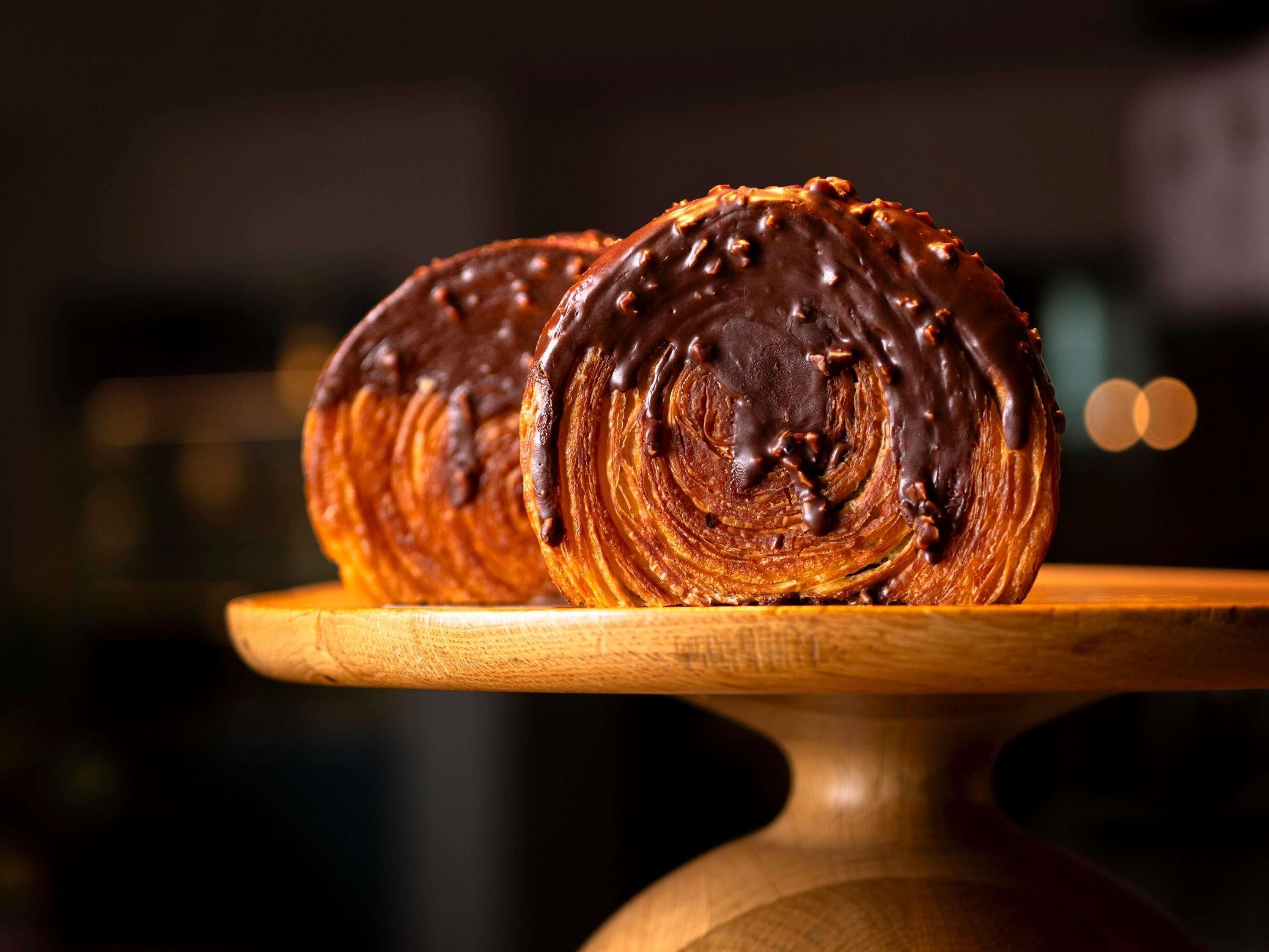 Dos bollos cubiertos de chocolate sobre un soporte de madera.