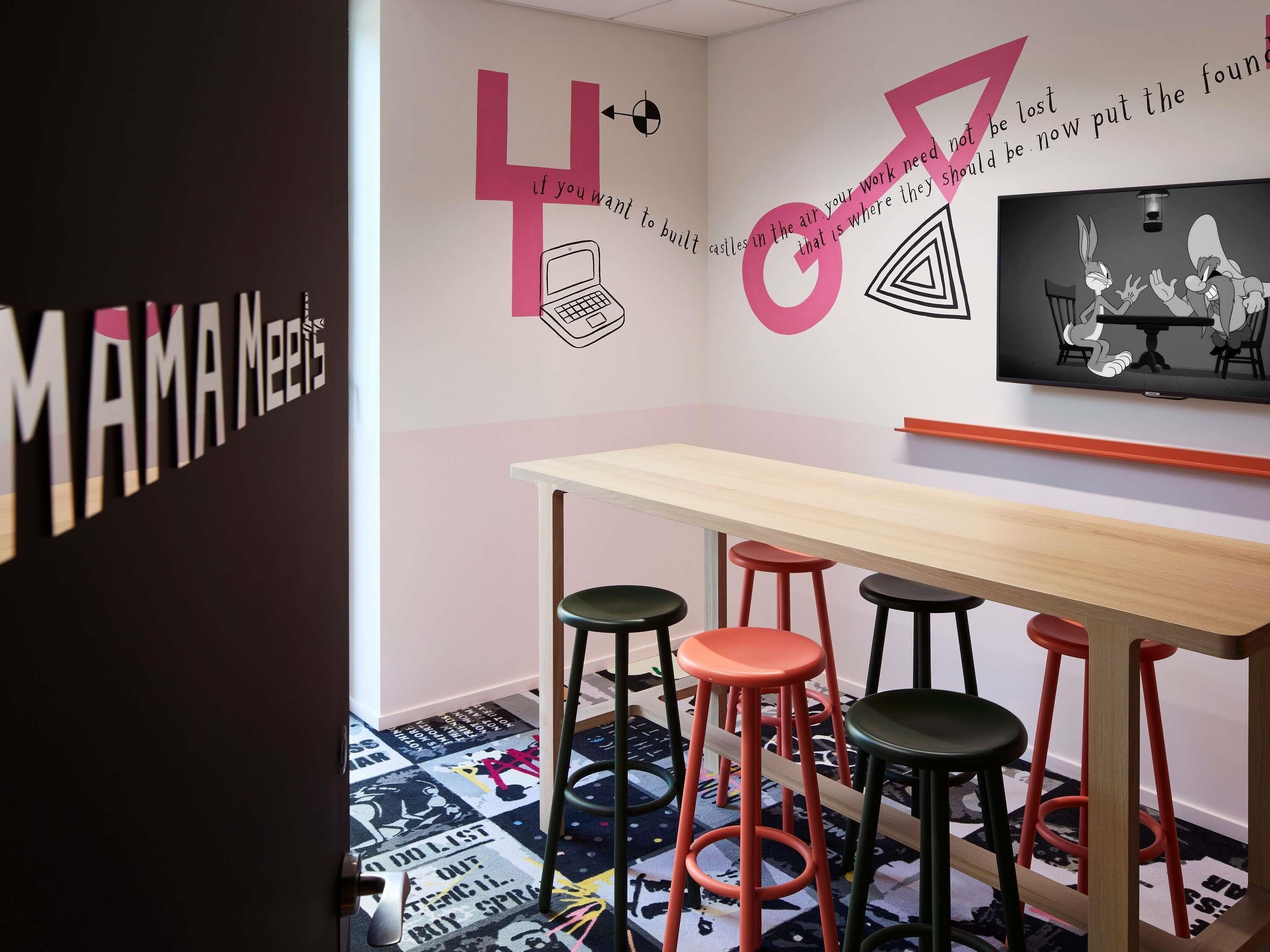 A modern room with a long table and four stools, a wall with motivational quotes, and a television displaying animated characters.