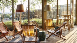 Een terras met lounge stoelen en tafels, grote ramen en uitzicht op de stad.