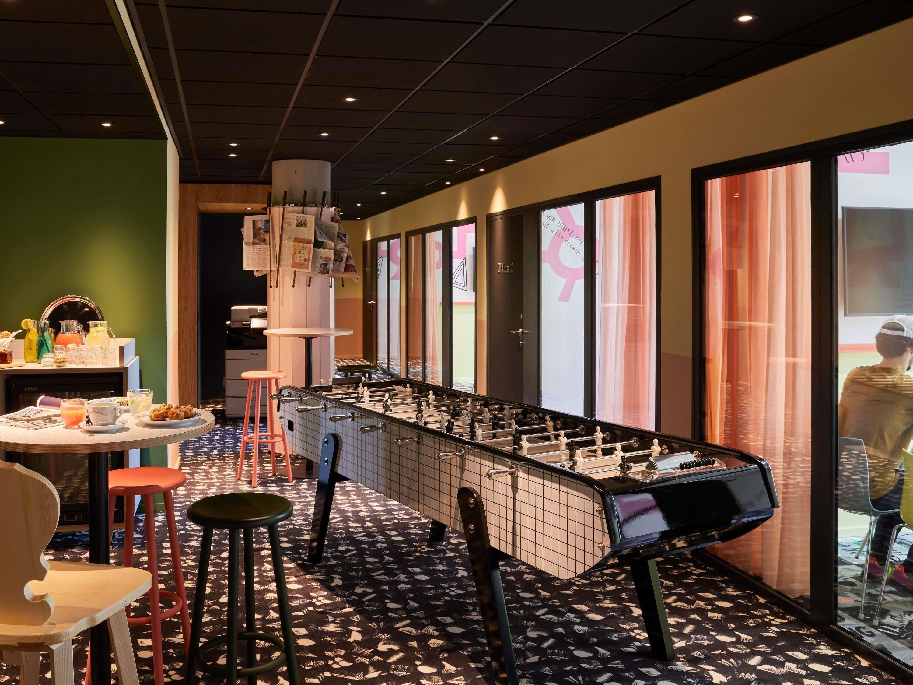 Ein Zimmer mit einem Kicker, einer Bar mit Hockern sowie einer Frühstücksecke mit verschiedenen Getränken und Speisen.