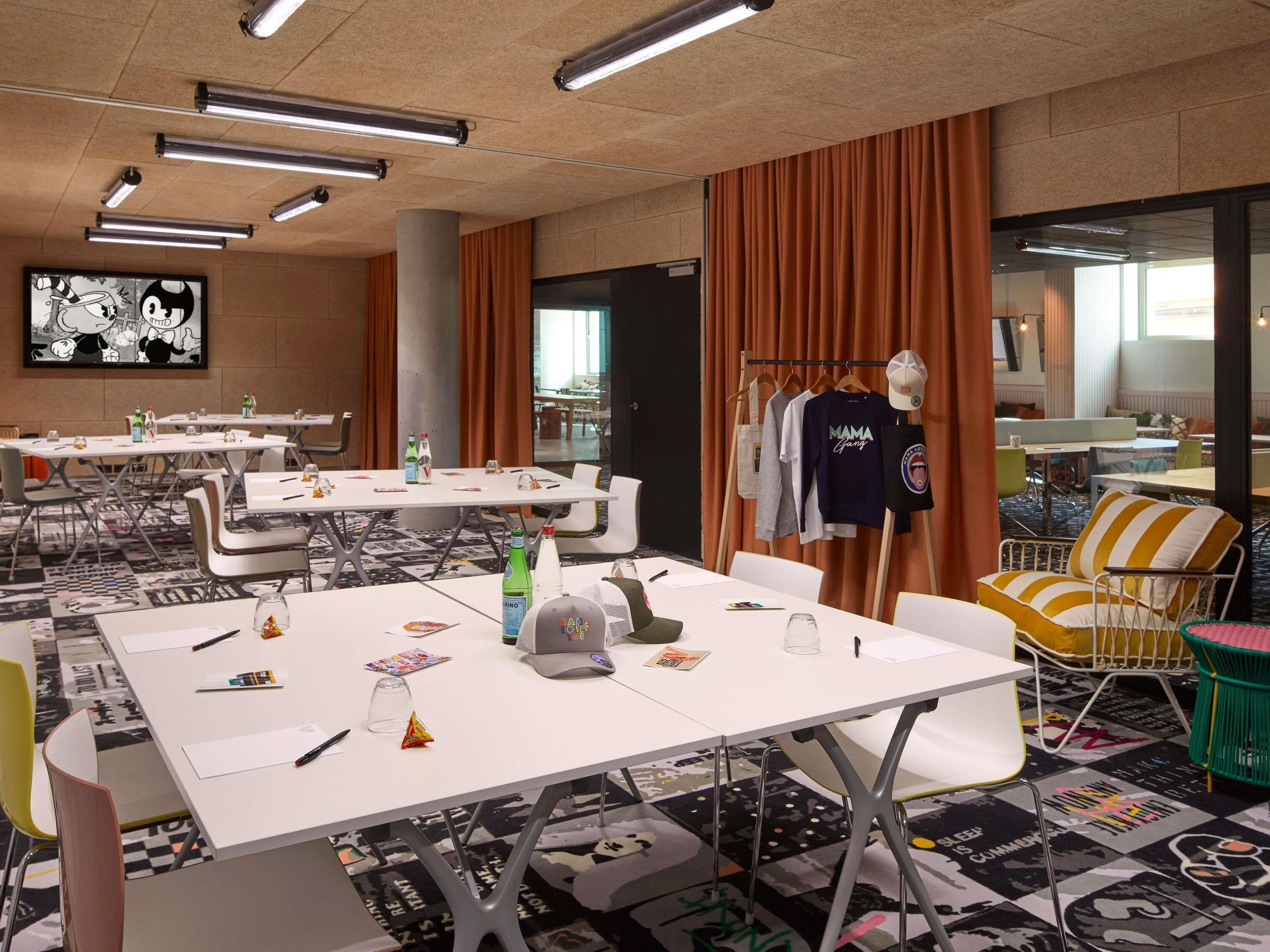Une salle de conférence équipée de tables, de chaises, d’un téléviseur et d’un portant à vêtements.