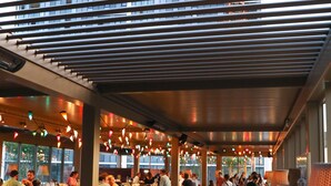 Een eethoek binnen met meerdere tafels en stoelen, een bar en uitzicht op buiten door grote ramen.