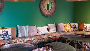 Una habitación con pared verde, un sofá con cojines estampados, una mesa redonda y lámparas colgantes.