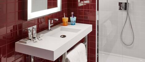 Un baño moderno con lavamanos blanco, paredes de azulejos rojos, cabina de ducha de vidrio y un perchero para toallas.