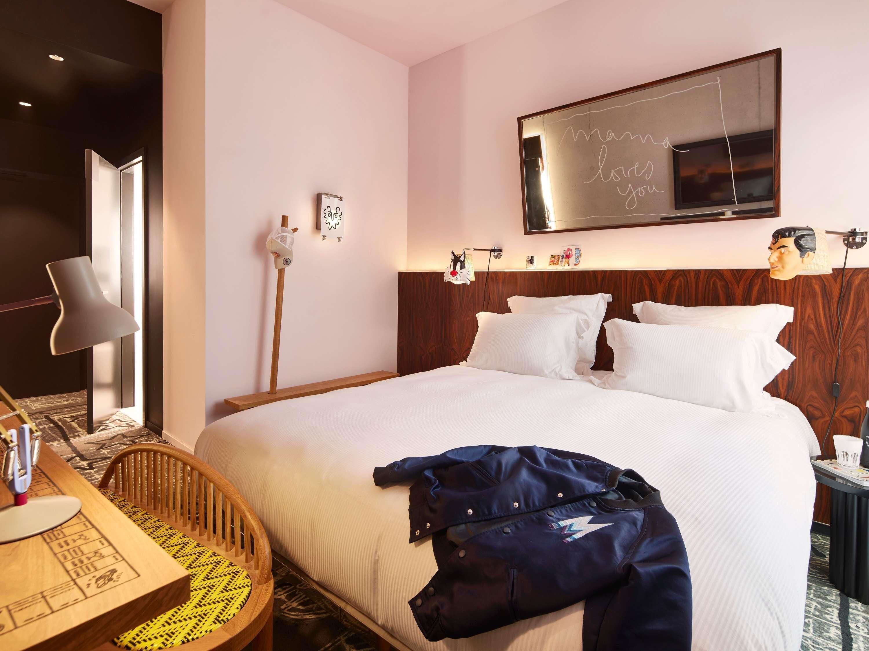Una habitación de hotel con una cama, un escritorio con lámpara, una silla y un televisor montado en la pared.