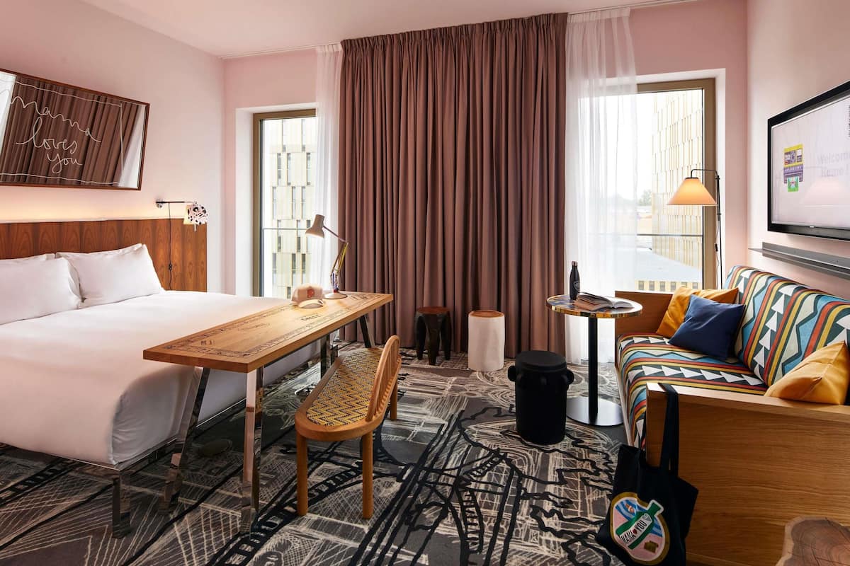 A hotel room with a bed, a desk, a chair, a sofa, a TV, and a window with curtains.
