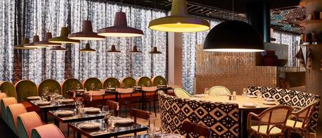 A restaurant with multiple tables, chairs, and hanging pendant lights.