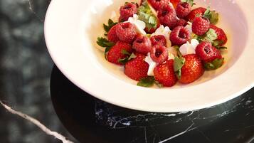 A white bowl with a salad of strawberries and raspberries on a black marble surface.