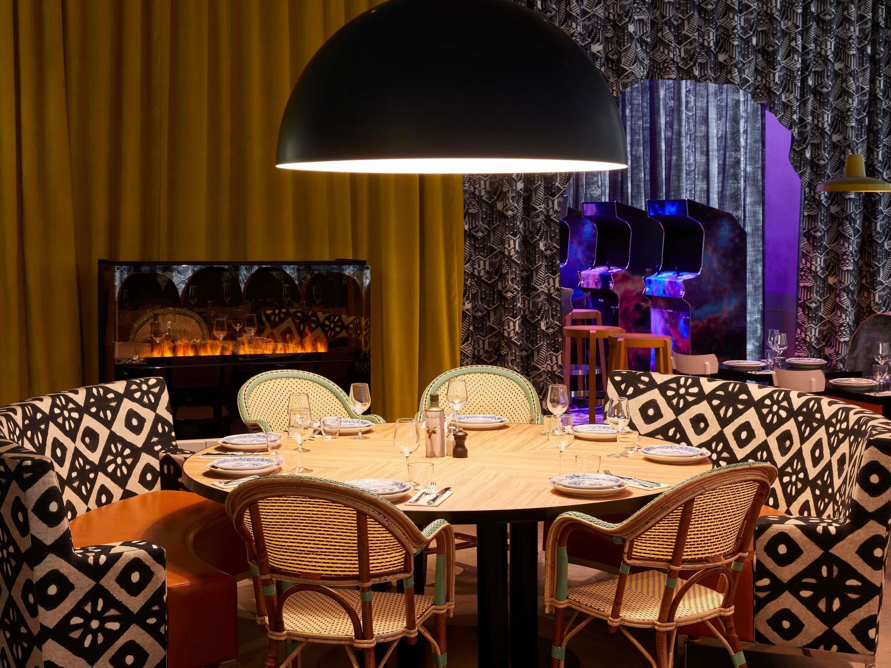 A dining area with a round table, wicker chairs, and a large black pendant light.