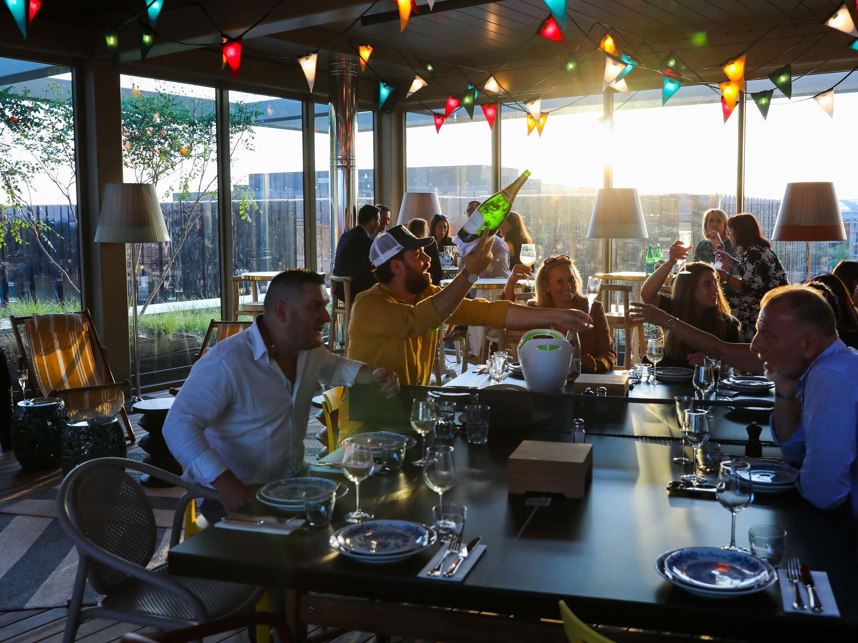 An outdoor dining area with tables set for a meal, surrounded by large windows and a view of the outdoors.