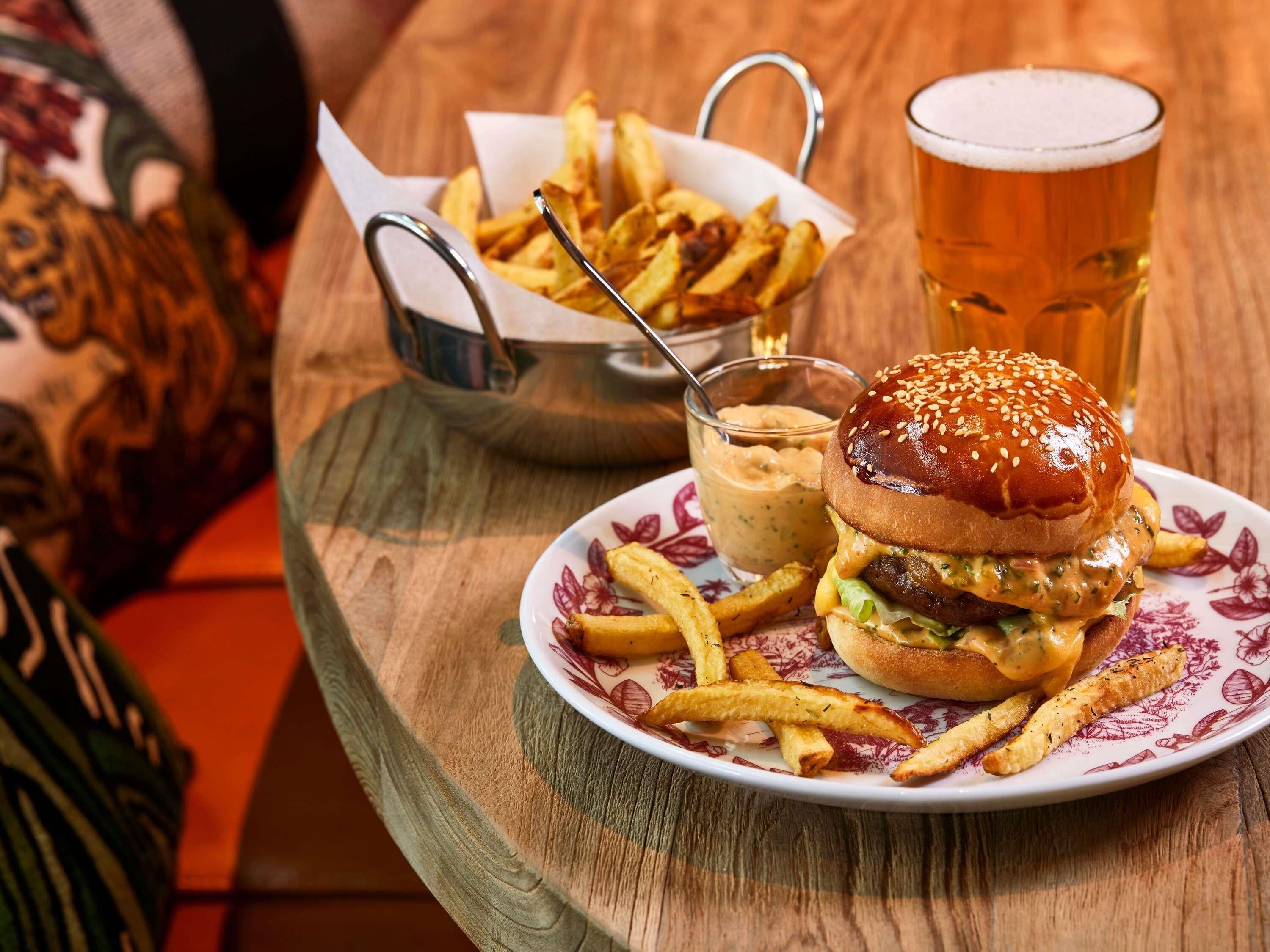 Une assiette contenant un hamburger, des frites et une boisson, posée sur une table en bois.