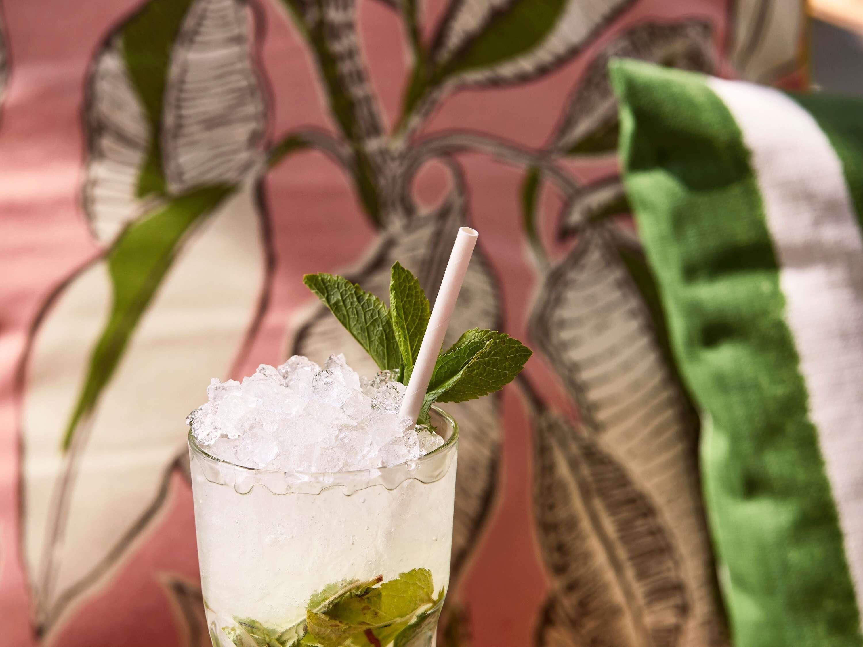 Un vaso con pajita, hielo y hojas de menta.