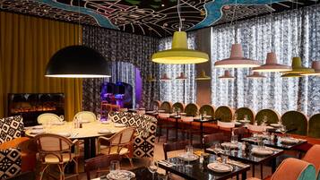 Un restaurante con una decoración moderna, que destaca por un papel tapiz estampado, arte único en el techo y diversas opciones de asientos.