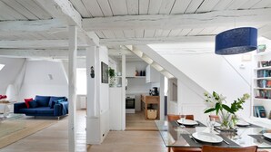 Ein geräumiger Loft mit hohen Decken, einem Essbereich mit Glastisch und einer gemütlichen Wohnstube mit blauem Sofa.