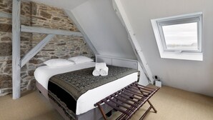 Ein Schlafzimmer mit Steinwand, einem Bett mit gemustertem Überwurf, einer Holzbank und einem Fenster mit Blick.