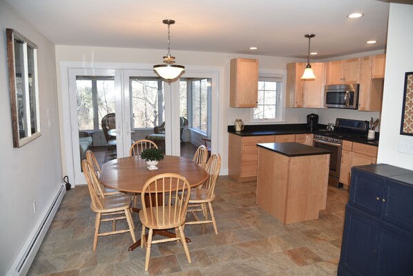 A modern kitchen with wooden cabinets, a central island, and a dining area with a round table and chairs.