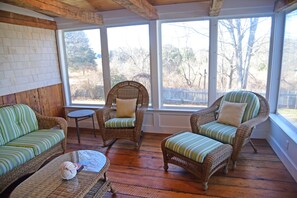 A sunroom with wicker furniture, large windows, and a wooden floor.