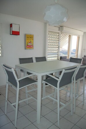 Un comedor con una mesa y sillas blancas, una lámpara de techo y un ventanal con persianas.