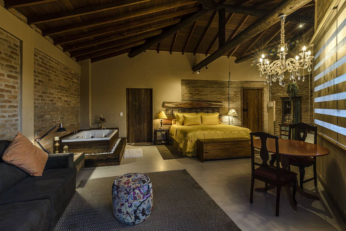 Ein gemütliches Schlafzimmer mit einem großen Bett, einem Holzkopfteil, einer Chandelüster und einer Ziegelwand.