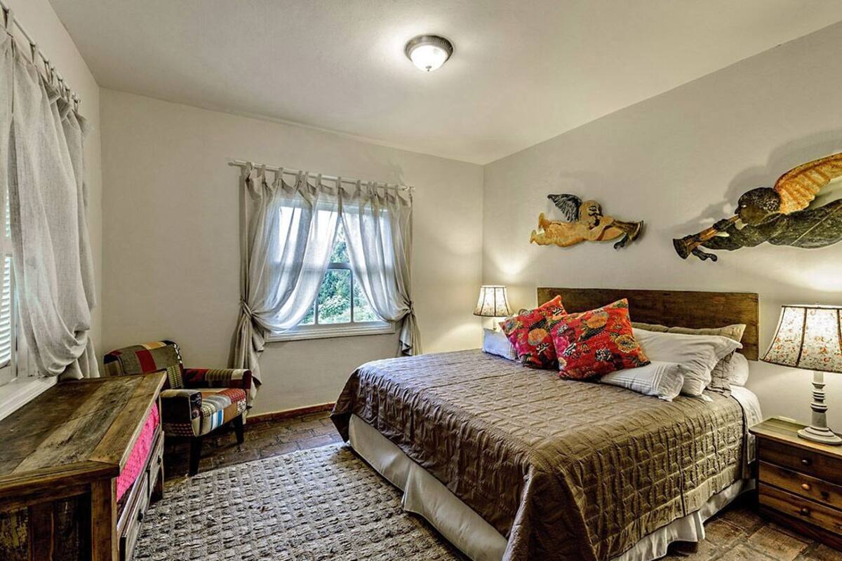 Ein Schlafzimmer mit Bett, Nachttischen, einem Fenster mit Vorhängen, einem Teppich und Wanddekorationen.