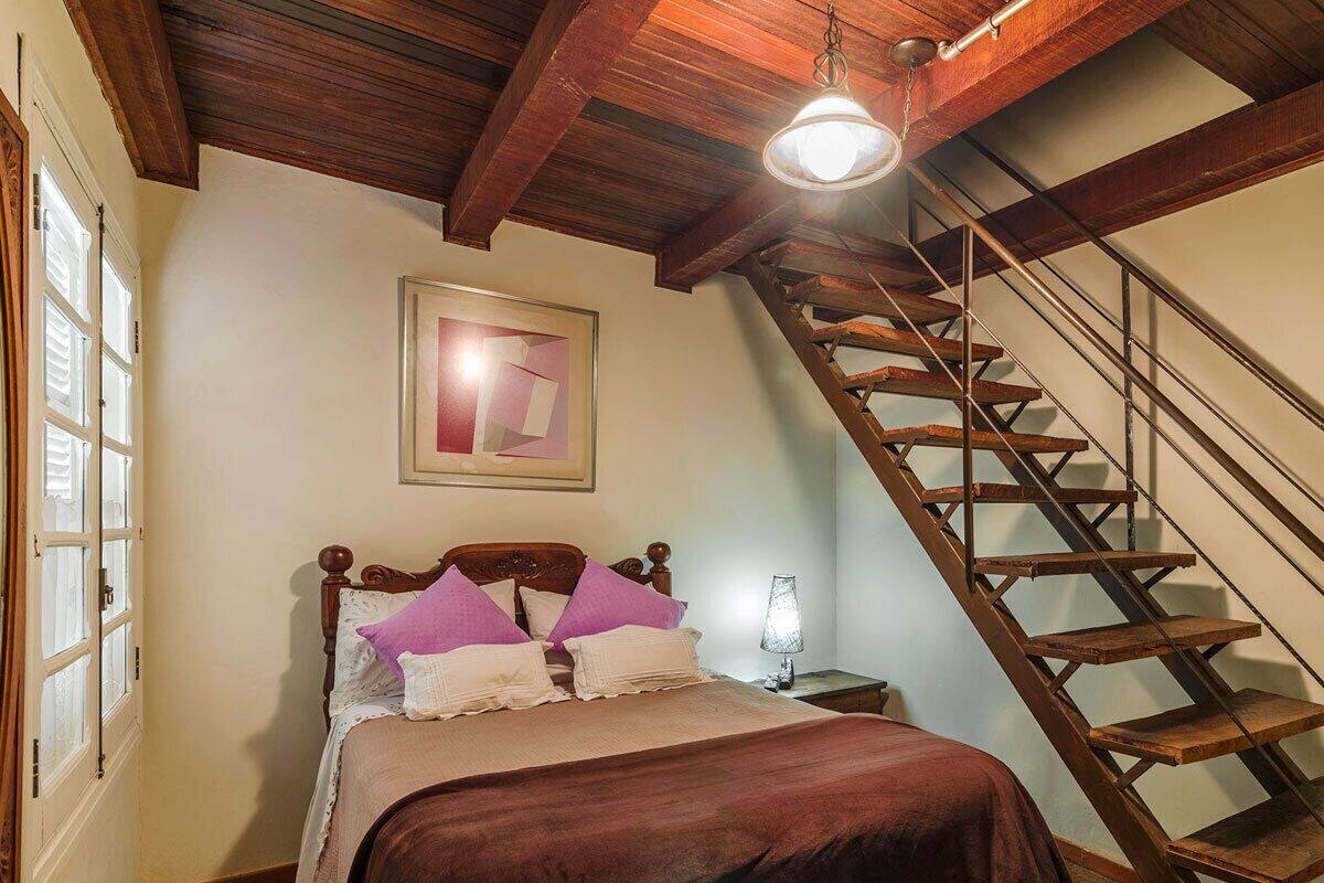 Ein Schlafzimmer mit einem hölzernen Bett, einem Nachttisch, einer Lampe, einem Bild an der Wand und einer Holztreppe.