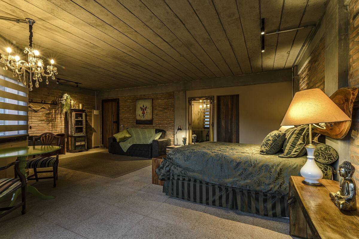 Ein gemütliches Schlafzimmer mit Bett, Holz-Kopfteil, Nachttisch, Lampe und einer Deckenleuchte.