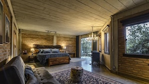 A modern bedroom with a large bed, a sofa, a chandelier, and a view of the outdoors.