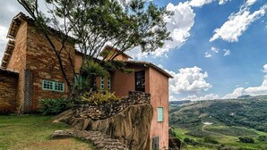 A rustic house with a stone staircase, a small garden, and a view of rolling hills.