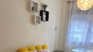A yellow sofa with striped pillows, a small side table, a potted plant, and a dining area with a glass table and chairs. - K2 2-bedroom apartment (Cáceres)
