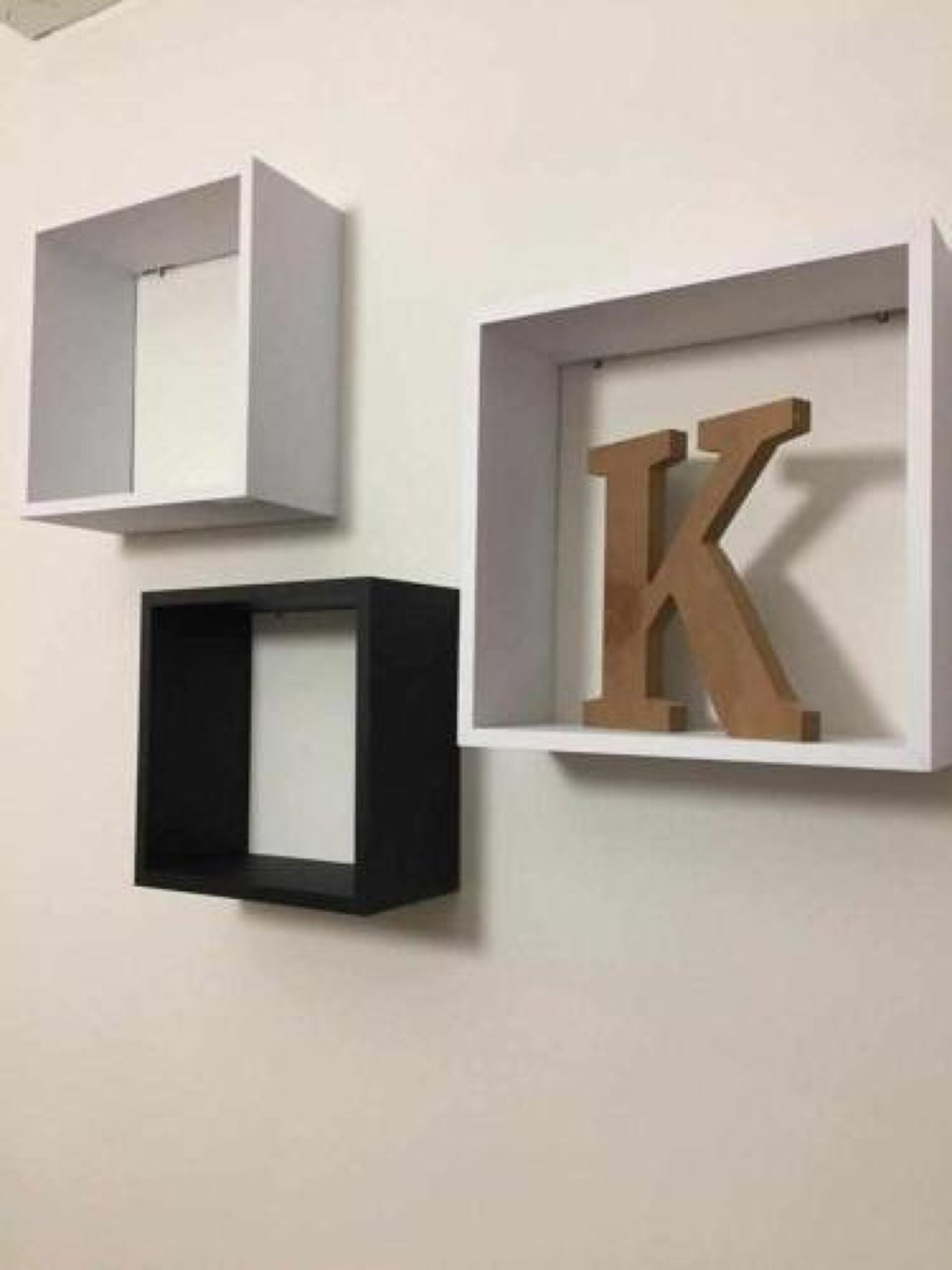 Three framed objects on a wall: two empty frames and one with a large letter 'K'.