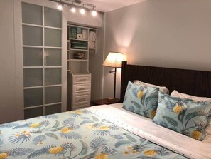 Un dormitorio con cama, mesita de noche, lámpara, armario con cajones y ventana con cortinas.