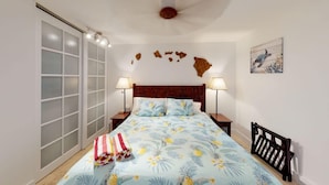 Un dormitorio con cama, dos mesitas de noche, cabecera de madera, ventilador de techo, una obra de arte colgada en la pared y una puerta corredera de vidrio.
