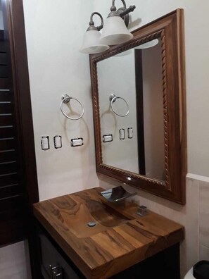 A bathroom with a wooden vanity, a mirror with a decorative frame, and wall-mounted towel rings.