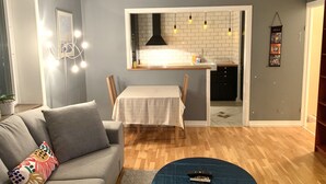 Ein Wohnzimmer mit grauem Sofa, einem Esstisch und einer Küchenzeile mit weiß gefliestem Rücksprühefeld und Pendelleuchten.