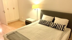 Ein ordentlich bezogenes Bett mit einem gemusterten Überwurf, zwei Kissen, einem Nachttisch, einer Lampe und einem Kleiderschrank.
