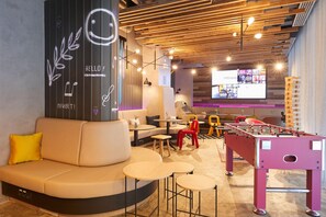 A modern lounge area with a foosball table, sofas, and a projection screen displaying images. - Moxy Bucharest Old Town (Bucharest)