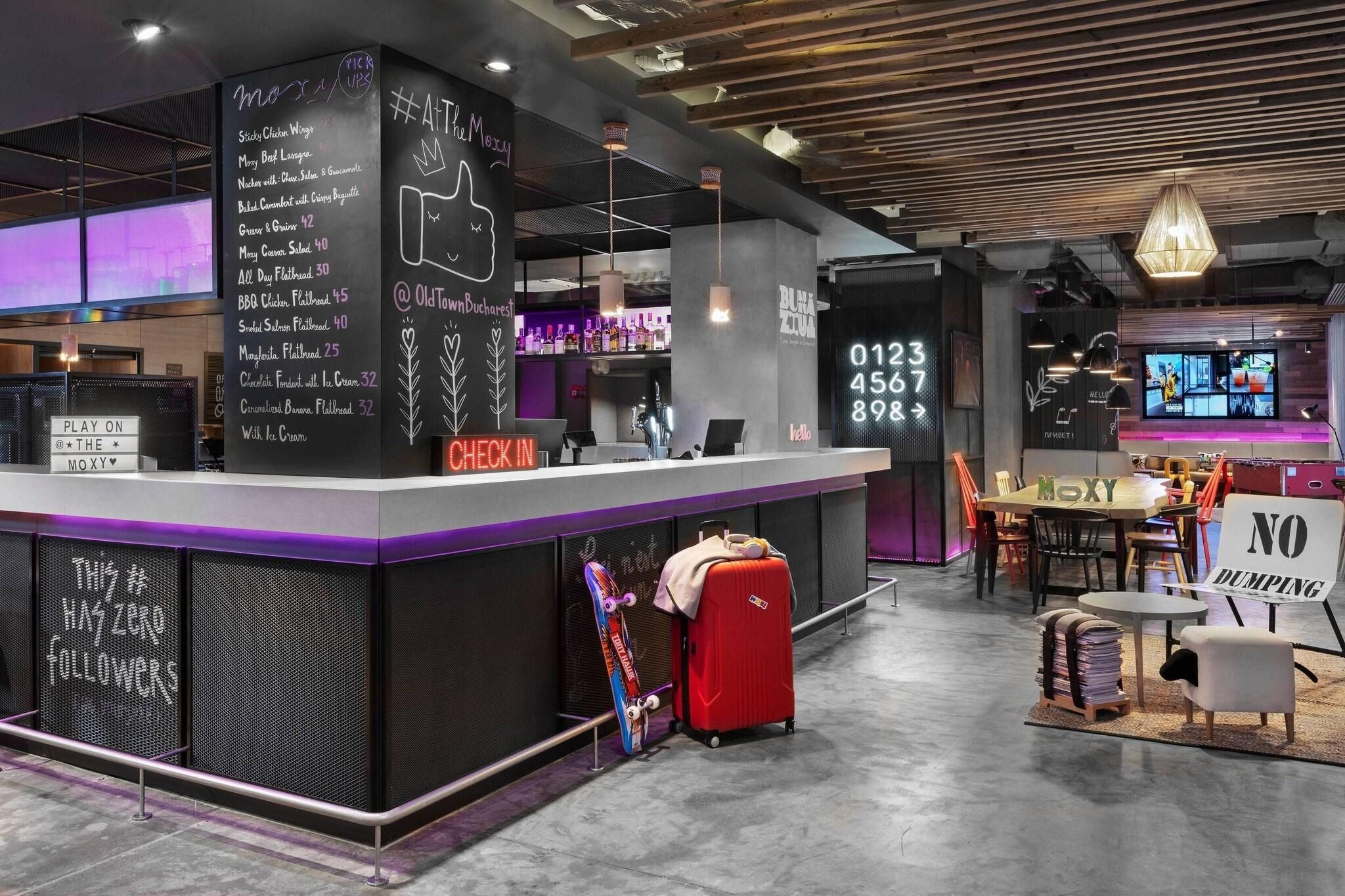 A modern bar area with a check-in counter, seating, and a digital display.